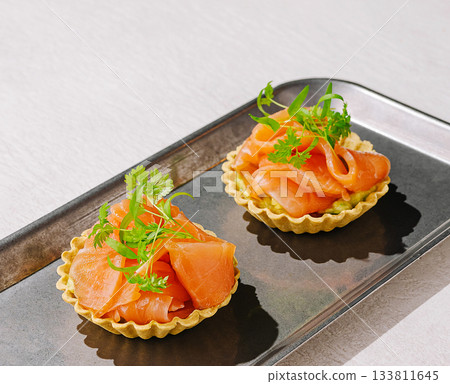 Delicate salmon tartlets served on a sleek metal tray Delicate salmon tartlets served on a sleek metal tray 133811645