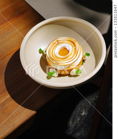 Delicate dessert with creamy topping and mint leaves on a wooden table Delicate dessert with creamy topping and mint leaves on a wooden table 133811647