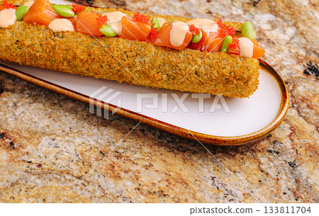 Delicious sushi roll topped with salmon and vegetables on a decorative plate Delicious sushi roll topped with salmon and vegetables on a decorative plate 133811704
