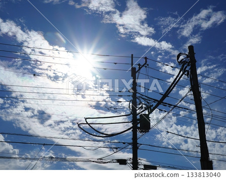 A landscape with the sun, clouds, and electric poles. The sun is dazzling. Copy space. Very beautiful. 133813040