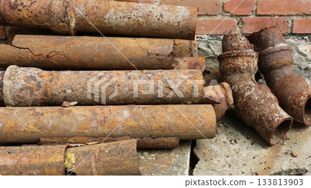 Rusty water pipes lying on the ground near a brick wall, used corroded iron, replacement of drainage pipes, dismantling old rotten pipes covered with a layer of rust, oxidation of metal water pipes 133813903