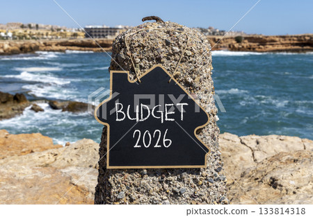 Budget 2026 symbol. Concept words Budget 2026 on beautiful black blackboard. Beautiful stone sea and blue sky background. Business and budget 2026 concept. Copy space. Budget 2026 symbol. Concept words Budget 2026 on beautiful black blackboard. Beautiful stone sea and blue sky background. Business and budget 2026 concept. Copy space. 133814318