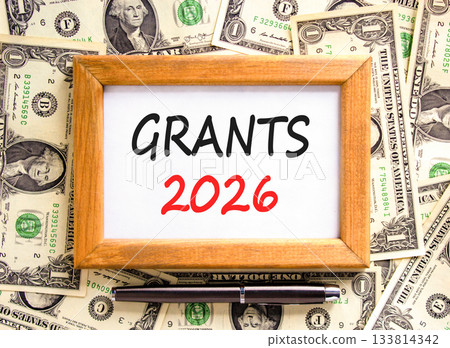 Grants 2026 symbol. Concept words Grants 2026 on beautiful wooden picture frame. Beautiful dollar bills background. Black pen. Dollar bills. Business and grants 2026 concept. Copy space. 133814342