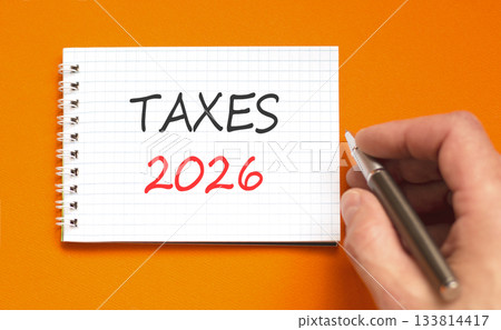Taxes 2026 new year symbol. Concept words Taxes 2026 on beautiful white note. Beautiful orange paper background. Businessman's hand with pen. Business and taxes 2026 new year concept. Copy space. 133814417