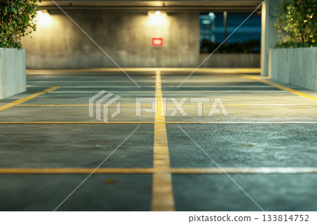Quiet parking lot at night featuring clear yellow lines and warm lights casting shadows on the pavement surface 133814752