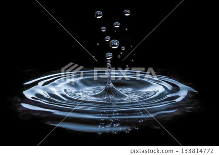 Droplets of water are captured mid-air as they splash into a still surface, forming beautiful ripples in a dark background Droplets of water are captured mid-air as they splash into a still surface, forming beautiful ripples in a dark background 133814772