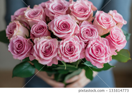 A person is holding a vibrant bouquet of pink roses with soft petals indoors, showcasing their elegant beauty and fresh appearance 133814773