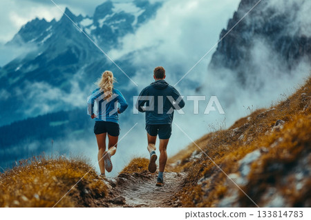 Two runners traverse a rugged mountain path surrounded by towering peaks and mist, enjoying an early morning jog Two runners traverse a rugged mountain path surrounded by towering peaks and mist, enjoying an early morning jog 133814783