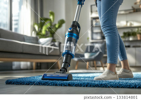 A person is cleaning a blue carpet using a vacuum cleaner in a stylish living room filled with plants and contemporary furniture A person is cleaning a blue carpet using a vacuum cleaner in a stylish living room filled with plants and contemporary furniture 133814801