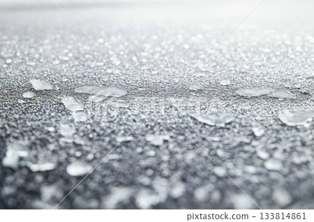 Morning frost creates a shimmering layer of ice shards on a dark surface, reflecting the soft light of dawn Morning frost creates a shimmering layer of ice shards on a dark surface, reflecting the soft light of dawn 133814861