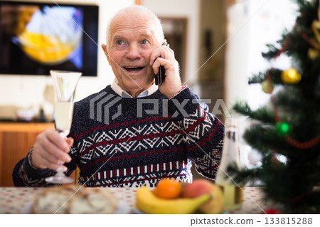 Elderly man wishes Merry Christmas by phone to friends and acquaintances sitting at the festive table in house Elderly man wishes Merry Christmas by phone to friends and acquaintances sitting at the festive table in house 133815288