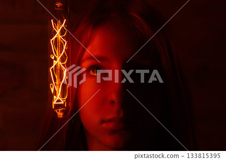 A moody portrait featuring a young woman's face dramatically illuminated on one side A moody portrait featuring a young woman's face dramatically illuminated on one side 133815395