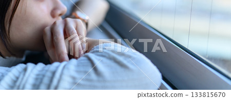 Close-up of a young woman's profile lost in thought by the window 133815670