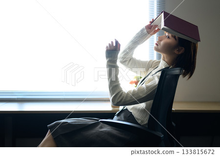 A young woman relaxing on a desk with a book on her head A young woman relaxing on a desk with a book on her head 133815672