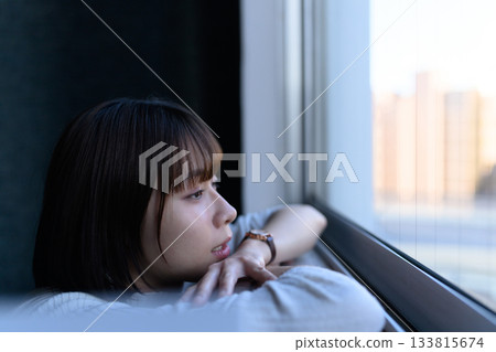 A melancholic portrait of a woman in her twenties lost in thought by the window 133815674