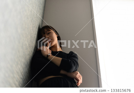 A young woman leaning against a wall with a melancholic expression 133815676