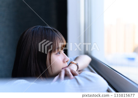 一位年輕女子側臉凝視窗外，陷入沉思。 133815677