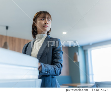 一位年輕的日本女商務人士在辦公室拿著文件，凝視著遠方。 133815678