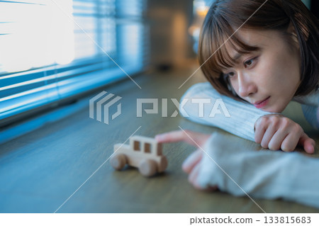 一位年輕女子深情地凝視著窗邊的一輛木製玩具車。 133815683