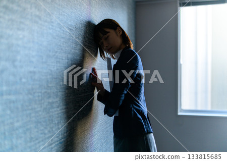 一位身著職業套裝、神情憂慮的年輕女子倚靠在牆上。 133815685