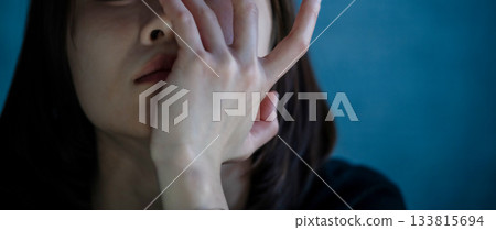 深藍色背景上，女人的雙手摀著臉。 133815694