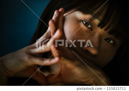 黑暗中,一位年輕女子用手指比劃出一個心形,鏡頭特寫她的臉。 黑暗中,一位年輕女子用手指比劃出一個心形,鏡頭特寫她的臉。 133815711
