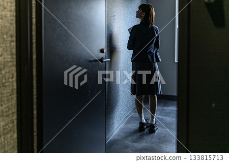 一位女子背對著鏡頭，站在昏暗走廊的一扇門前。 133815713