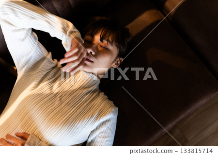 年輕女子躺在沙發上休息，閉著眼睛放鬆身心。 133815714