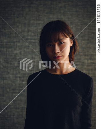 一位表情嚴肅的年輕日本女性站在深色背景前的肖像。 133815716