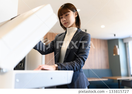 A young female business person operating a multifunction printer in the office 133815727