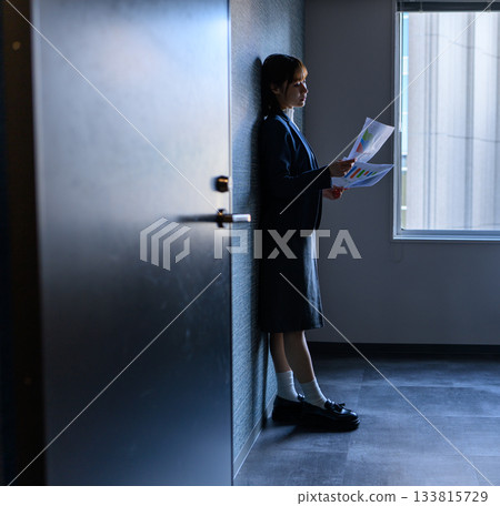 A young female business person in a suit looking at documents in the hallway 133815729