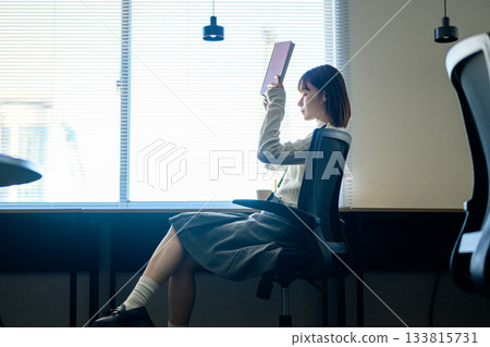 A young Japanese female employee reading a book by the window during a break 133815731