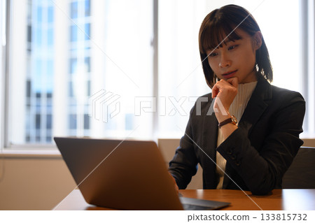A young Japanese female business person in a suit concentrating on a laptop 133815732