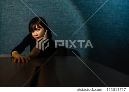 Pensive young woman leaning her elbows on a table in a dark room 133815737