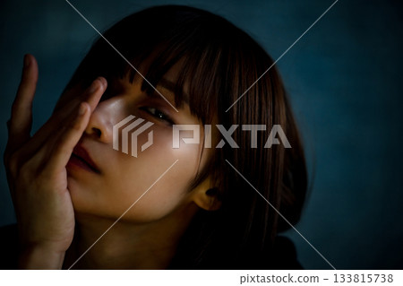 黑暗中，一位二十多歲女性的上半身肖像，她神情沮喪，半遮著臉。 133815738