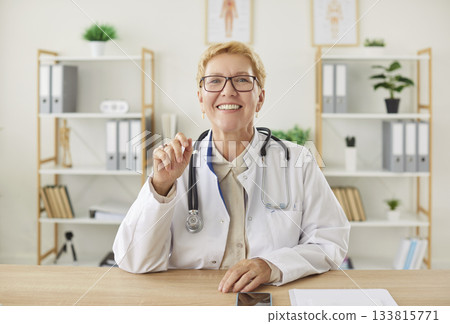 Portrait medical woman doctor talking online with patient, making video call, looking at camera Portrait medical woman doctor talking online with patient, making video call, looking at camera 133815771