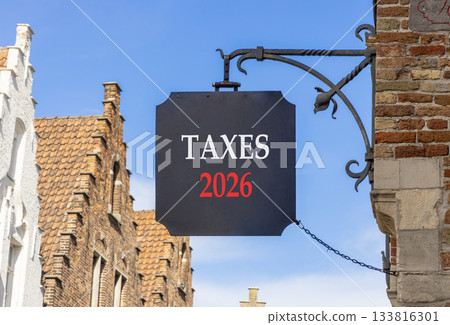 Taxes 2026 new year symbol. Concept words Taxes 2026 on beautiful black road sign. Beautiful street and buildings in Brugge blue sky background. Business and taxes 2026 new year concept. Copy space. Taxes 2026 new year symbol. Concept words Taxes 2026 on beautiful black road sign. Beautiful street and buildings in Brugge blue sky background. Business and taxes 2026 new year concept. Copy space. 133816301