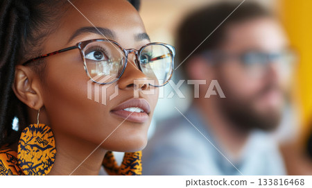 Black woman wearing glasses and African-inspired earrings leading discussion with white male colleague in tech-style office 133816468