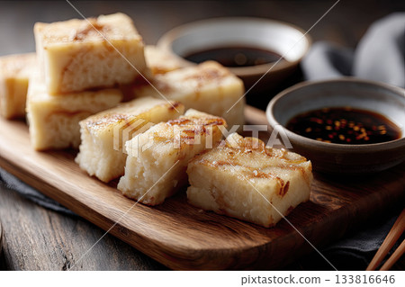 Slices of steamed turnip cake on a wooden board, soy dipping sauce nearby, simple Cantonese New Year atmosphere 133816646