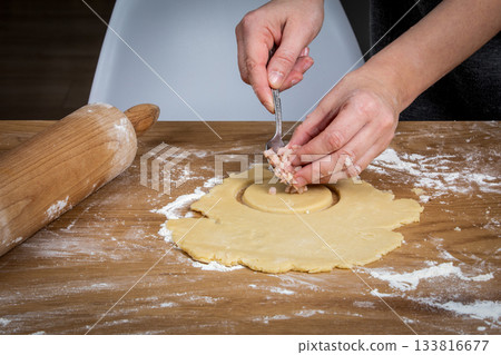Hands Adding Meat Filling to Dough Circle on Floured Wooden Surface 133816677
