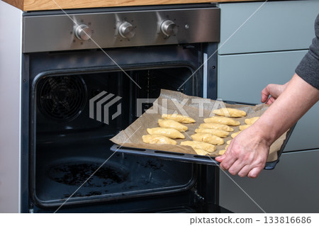 Placing Tray of Unbaked Pastries Into Open Oven in Home Kitchen Placing Tray of Unbaked Pastries Into Open Oven in Home Kitchen 133816686