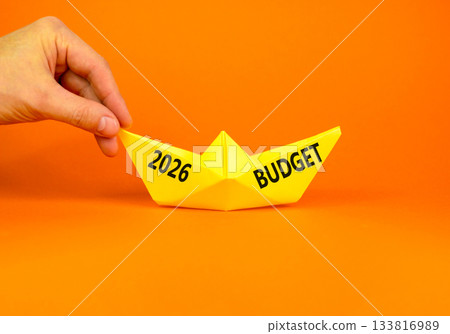 2026 Budget symbol. Concept words 2026 Budget on beautiful yellow paper boat. Beautiful orange paper background. Businessman's hand. Business and 2026 budget concept. Copy space. 2026 Budget symbol. Concept words 2026 Budget on beautiful yellow paper boat. Beautiful orange paper background. Businessman's hand. Business and 2026 budget concept. Copy space. 133816989