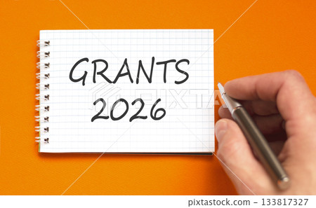 Grants 2026 symbol. Concept words Grants 2026 on beautiful white note. Beautiful orange paper background. Businessman's hand with pen. Business and grants 2026 concept. Copy space. Grants 2026 symbol. Concept words Grants 2026 on beautiful white note. Beautiful orange paper background. Businessman's hand with pen. Business and grants 2026 concept. Copy space. 133817327