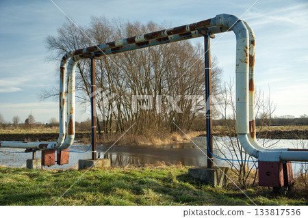 Rusting district heating pipes arched over a flooded field entrance 133817536