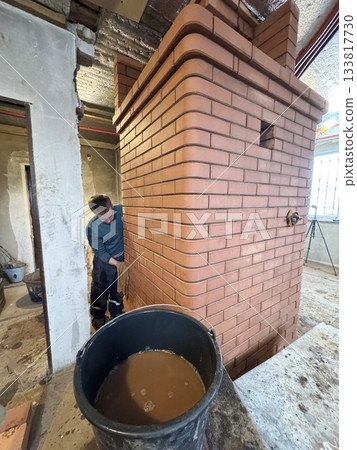Construction of a heating stove. The craftsman is washing the brickwork before handing over the project to the client. 133817730