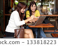 Two Asian Women Collaborating with Laptop and Tablet in Modern Cafe 133818223