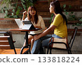 Two Asian Women Discussing Work with Laptop and Tablet in Cafe 133818224