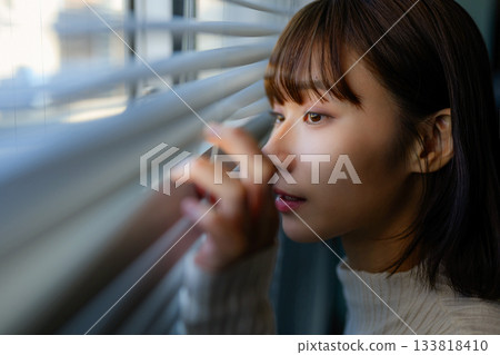 Portrait of a young woman peeking through the blinds 133818410