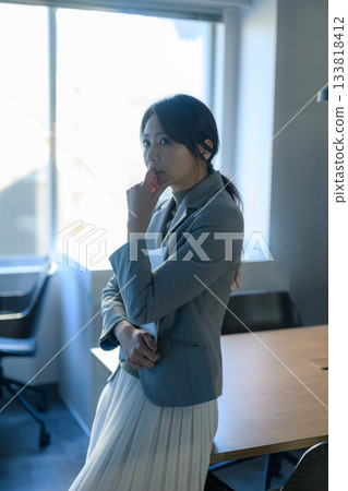 A Japanese businesswoman in a suit thinking by the window A Japanese businesswoman in a suit thinking by the window 133818412
