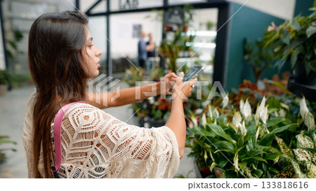 A young woman passionately taking beautiful photos among a variety of stunning indoor plants A young woman passionately taking beautiful photos among a variety of stunning indoor plants 133818616